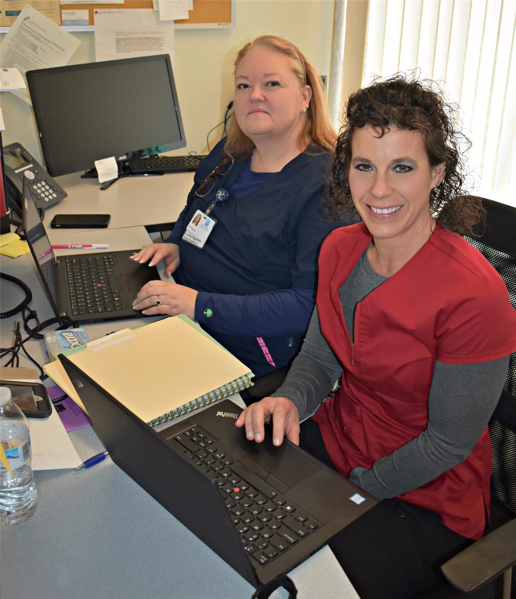 Two nurses sitting in front of computer getting picture taken